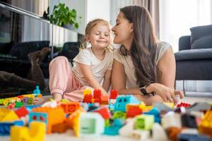 pequeño niña jugar con constructor juguete en piso en hogar con mamá o mujer niñera, educativo juego, familia a hogar gastar ocio ocupaciones hora juntos concepto foto