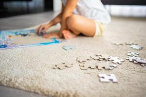 Little blonde girl sits at home on the carpet and collects puzzles. Focus on the puzzle pieces photo