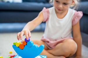 Little girl playing with wooden balancing toy on the floor in home living room. Focus on balancer photo