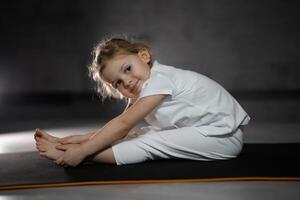 Little cute girl practicing yoga pose on grey background in dark room. High quality photo