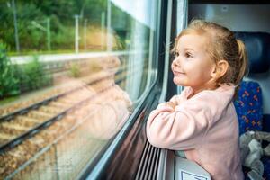 contento pequeño niña mirando fuera tren ventana afuera, mientras eso Moviente. de viaje por ferrocarril en Europa foto