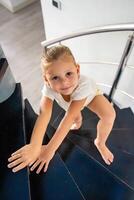 Portrait of little girl going up the stairs at home, child climbing spiral staircase. Dangerous situation at home. Child safety concept. photo