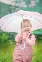 Happy laughing child girl 2-3 year old wearing waterproof clothes and holding pink umbrella have a fun on home backyard in rainy day photo