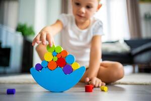 Little girl playing with wooden balancing toy on the floor in home living room. Focus on balancer photo