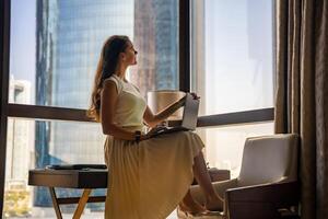 Stylish businesswoman freelancer with laptop sitting on the table and enjoying panoramic view in the city background. Low key photo. High quality photo