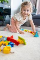 pequeño niña jugar con constructor juguete en piso en hogar, educativo juego, gasto ocio ocupaciones hora concepto foto