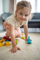 pequeño niña jugar con constructor juguete en piso en hogar, educativo juego, gasto ocio ocupaciones hora concepto foto