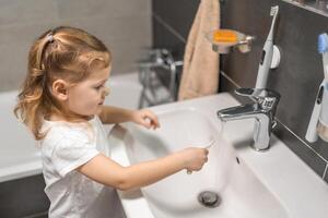 Happy toddler girl washing toothbrush after brushing teeth in the bath photo