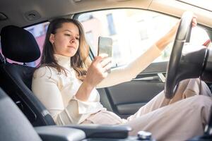 Young woman sitting in car and using smart phone, business woman busy driving photo