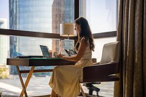 Stylish businesswoman freelancer working with laptop and she is sitting on the chair, enjoying panoramic view in the city background. Low key photo. High quality photo