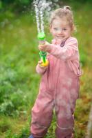 Happy laughing child girl 2-3 year old wearing waterproof clothes have a fun with water gun on home backyard photo