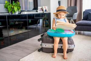 pequeño niña con maleta equipaje equipaje y inflable vida boya leyendo mapa y Listo a Vamos para de viaje en vacaciones foto