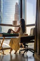 Stylish businesswoman freelancer working with laptop and sitting on chair, enjoying panoramic view in the city background. Low key photo. High quality photo