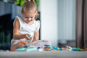 Smiling Little girl playing with small constructor toy on floor in home living room, educational game, spending leisure activities time concept photo