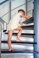 pequeño niña yendo arriba escalera a moderno hogar, niño alpinismo espiral escalera. peligroso situación a hogar. niño la seguridad concepto. foto