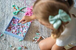 Little girl making wooden beads bracelet at home living room. Children's creativity and the development of fine motor skills photo