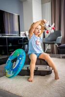 Little girl with suitcase baggage luggage and inflatable life buoy playing with toy plane and ready to go for traveling on vacation photo