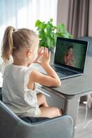 Little girl does finger gymnastics online on the laptop home. Distance learning concept. photo