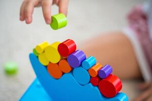 Little girl playing with wooden balancing toy on the floor in home living room. Focus on balancer photo