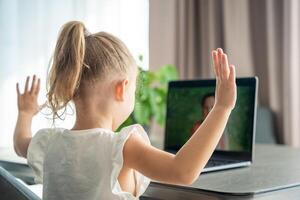 Little girl does finger gymnastics online on the laptop home. Distance learning concept. photo