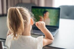 Little girl does finger gymnastics online on the laptop home. Distance learning concept. photo