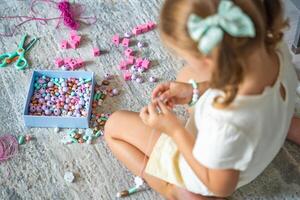 Little girl making wooden beads bracelet at home living room. Children's creativity and the development of fine motor skills photo