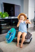 Little girl with suitcase baggage luggage and inflatable life buoy playing with toy camera and ready to go for traveling on vacation photo