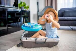 pequeño niña con maleta equipaje equipaje y inflable vida boya jugando con juguete cámara y Listo a Vamos para de viaje en vacaciones foto