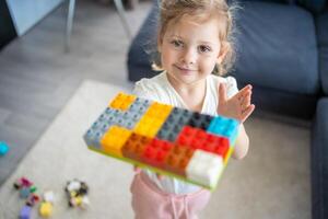 pequeño niña jugar con constructor juguete en piso en hogar, educativo juego, gasto ocio ocupaciones hora concepto foto