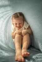 Little girl have a fun under blue knitted plaid in sunny morning photo