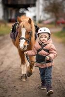 pequeño niña en protector chaqueta y casco con su marrón poni antes de montando lección. alto calidad foto