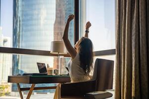 Stylish businesswoman freelancer with laptop stretching, she is sitting on the chair, enjoying panoramic view in window with city background. Low key photo. High quality photo