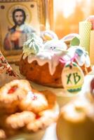 Easter cake with painted eggs, apples and cookies on table in home kitchen. Church icons and candle on background. Orthodox religion theme. High quality photo