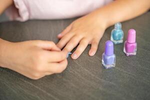 parte superior ver de manos de el pequeño niña haciendo manicura y pintura uñas con vistoso rosa, azul y púrpura uña polaco a hogar foto