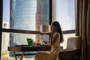 Stylish businesswoman freelancer working with laptop, she is sitting on the chair, enjoying panoramic view in city background. Low key photo. High quality photo