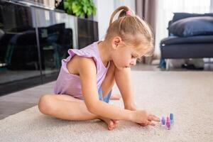 hermosa pequeño niña haciendo pedicure y pintura uñas con vistoso rosa, azul y púrpura uña polaco a hogar foto