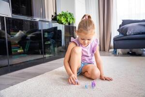 linda pequeño niña haciendo pedicure y pintura uñas con vistoso rosa, azul y púrpura uña polaco a hogar foto