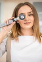 Portrait of blonde woman dermatologist with dermatoscope in uniform and gloves in doctor office before examination in clinic photo