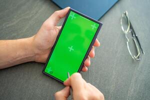 Close up view of man hand holding smart phone with green chroma key screen and stylus pen at his creative workspace photo