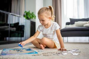 Little blonde girl sits at home on the carpet and collects puzzles. High quality photo