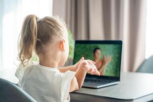 Little girl does finger gymnastics online on the laptop home. Distance learning concept. photo