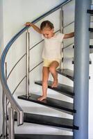 retrato de pequeño niña yendo abajo el escalera a hogar, niño alpinismo espiral escalera. peligroso situación a hogar. niño la seguridad concepto. foto