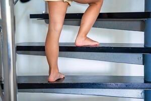 de cerca de pequeño niña pies yendo arriba el escalera a hogar, niño alpinismo escalera foto