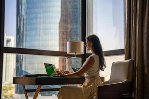 Stylish businesswoman freelancer working with laptop, she is sitting on the chair, enjoying panoramic view in the city background. Low key photo. High quality photo