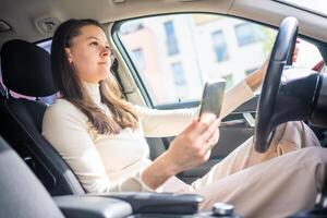 Young woman sitting in car and using smart phone, business woman busy driving photo