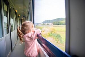 hermosa pequeño niña mirando fuera tren ventana afuera, durante de viaje. de viaje por ferrocarril, Europa foto