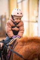 pequeño niño montando lección. tres años niña paseos un poni y lo hace ejercicios. alto calidad foto