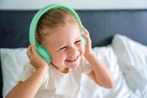 Smiling little girl emotional enjoying music using green kids headphones. High quality photo