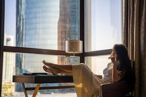 Stylish businesswoman freelancer working and she is laying on the chair, enjoying panoramic view in the city background. Low key photo. High quality photo