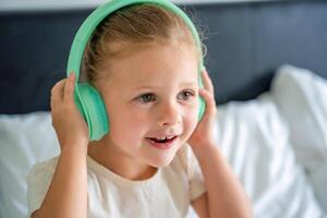 Little girl enjoying music using green kids headphones in home bed. High quality photo